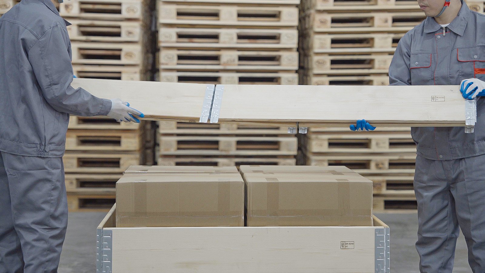 Workers placing plywood lid on pallet collar packed with cartons